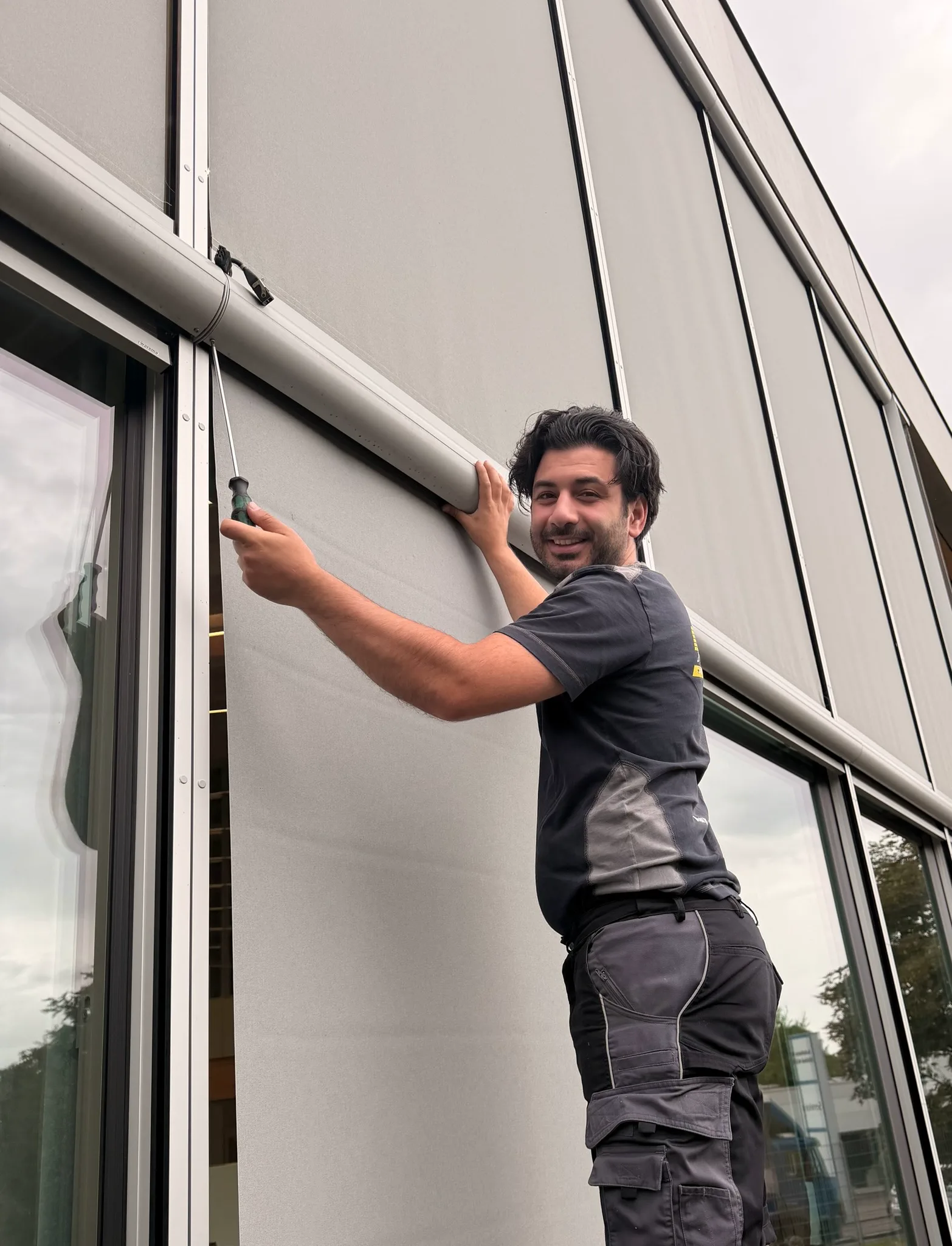 Techniker arbeitet mit einem Schraubendreher am Sonnenschutz über einem Fenster
